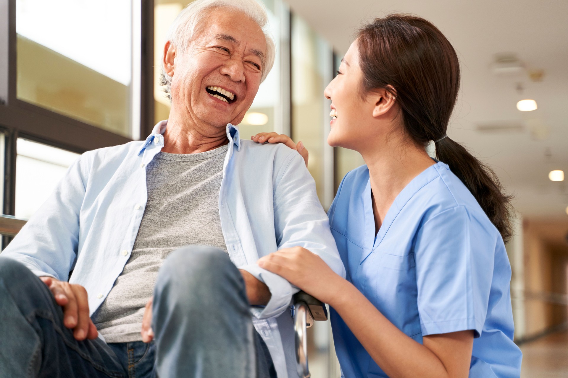 friendly asian caretaker talking to senior patient in nursing home